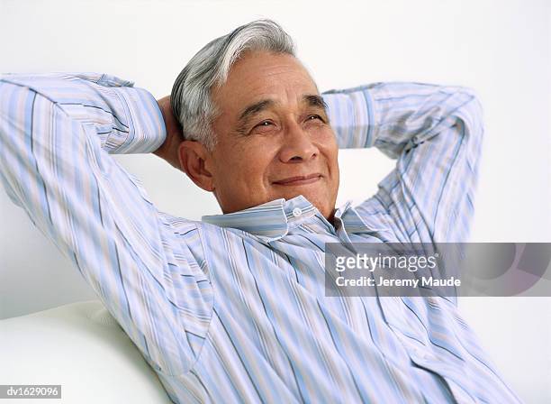 portrait of senior man relaxing on a sofa wth his hands behind his head - hands behind head stock pictures, royalty-free photos & images