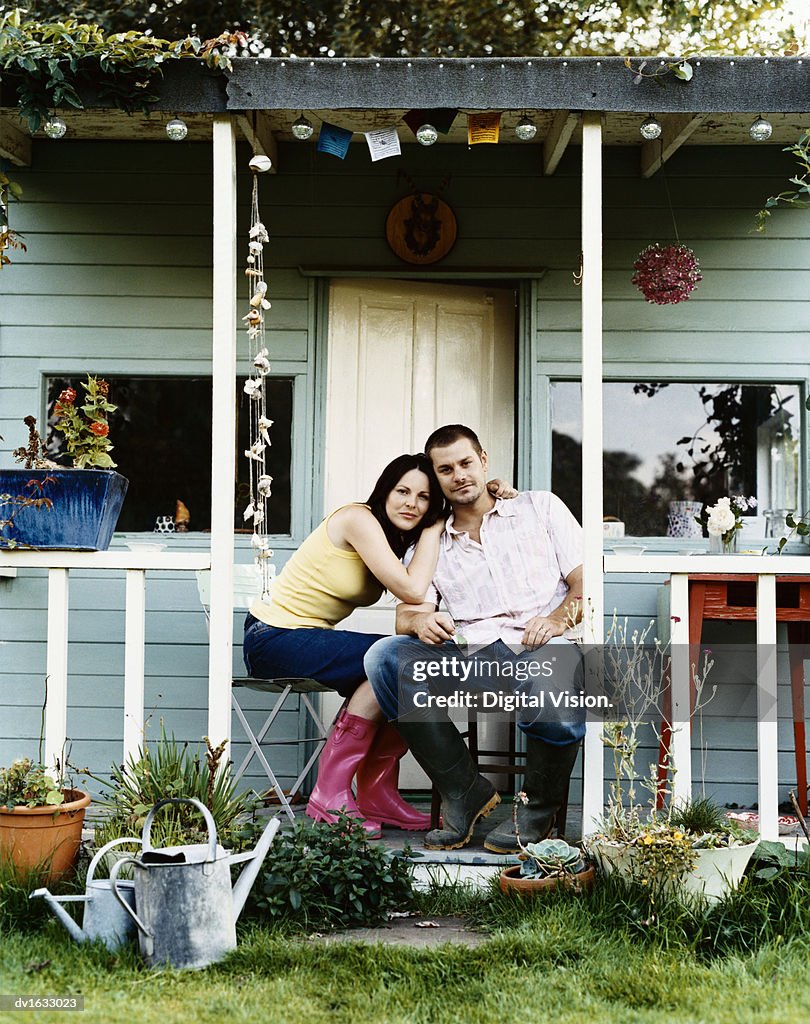 Couple Sit Side by Side on the Porch of Their Wooden Bungalow