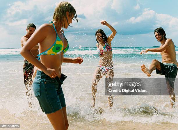 young men and women stand on the beach at the water's edge, kicking and splashing water at their friend - voyage15 photos et images de collection