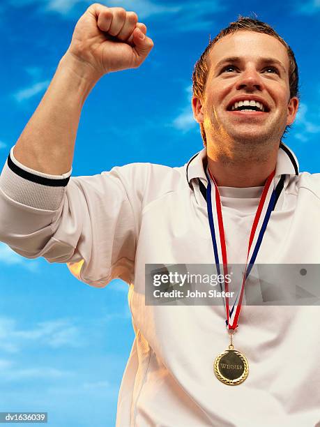 portrait of a male athlete wearing a gold medal and punching the air - tracksuit jacket stock pictures, royalty-free photos & images