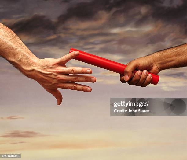 close-up on the hand of a male athlete passing a relay baton to another athlete, with a dramatic sky in the background - relay fotografías e imágenes de stock