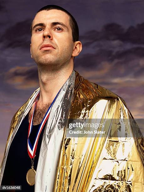 portrait of a male athlete wearing a gold medal and a golden foil blanket - noodapparatuur stockfoto's en -beelden
