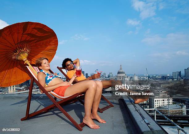 a man and woman relaxing on deck chairs on a roof with st pauls catherdral in the background - out of context foto e immagini stock
