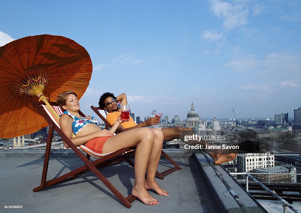 A Man and Woman Relaxing on Deck Chairs on a Roof with St Pauls Catherdral in the Background