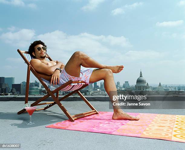 man relaxing in a deck chair on a roof against a london skyline - mens swimwear foto e immagini stock
