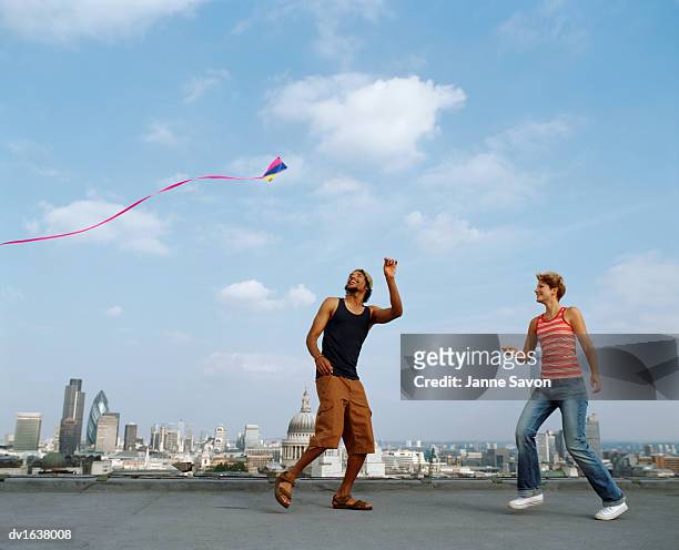 man and woman flying a kite on a roof against a skyline of london - nur erwachsene stock-fotos und bilder