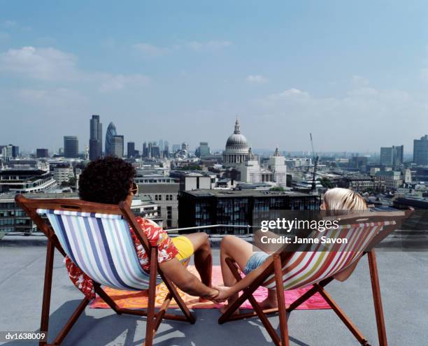 couple sitting in deck chairs and holding hands facing a skyline of london - out of context foto e immagini stock