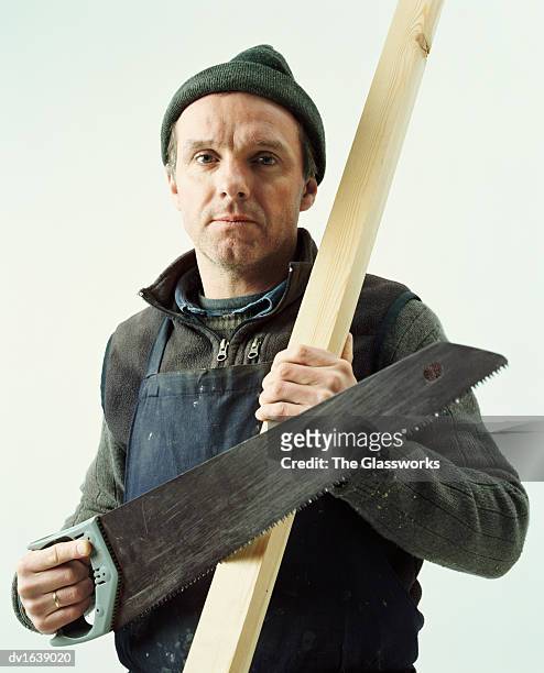 portrait of a male carpenter holding a piece of wood and a saw - male wool hat stock-fotos und bilder