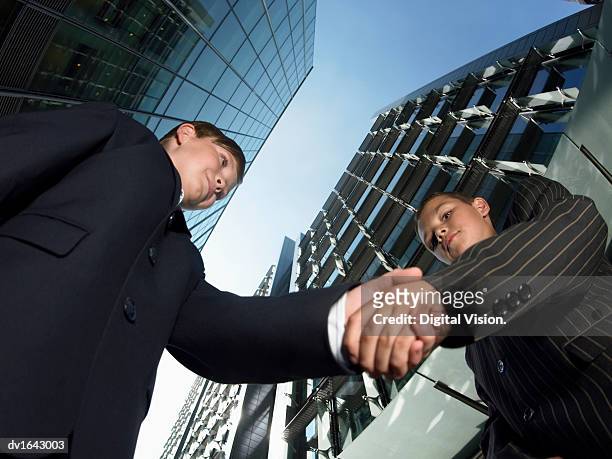 view directly below of two young boys dressed as businessmen standing next to skyscrapers, shaking hands - low angle view of two businessmen standing face to face outdoors stock pictures, royalty-free photos & images