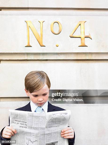 young boy dressed as a businessman reads a financial newspaper below a street number sign - renversement des rôles photos et images de collection