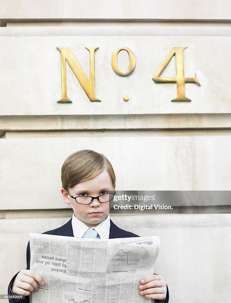 Young Boy Dressed as a Businessman Reads a Financial Newspaper Below a Street Number Sign