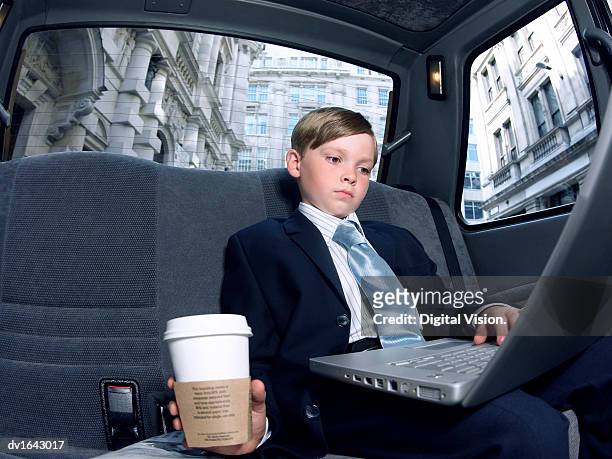 boy dressed as a businessman, sitting in a taxi using a laptop computer - crazy car fotografías e imágenes de stock
