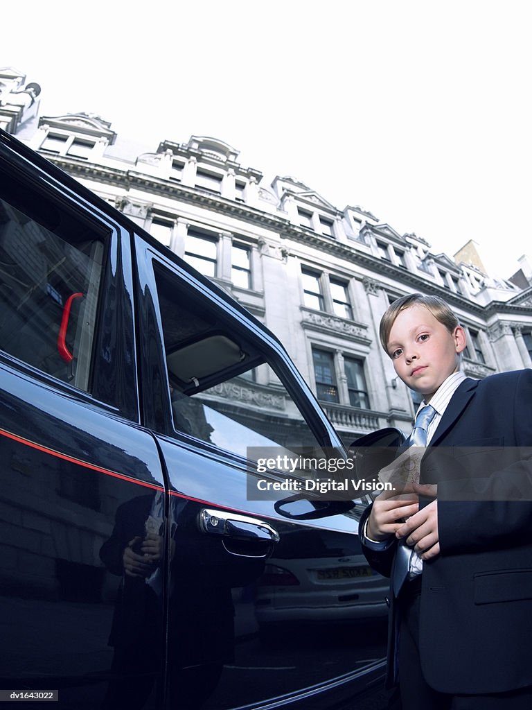 Boy Dressed as a Businessman Holding a Bundle of Ten Pound Notes, Standing next to a Taxi