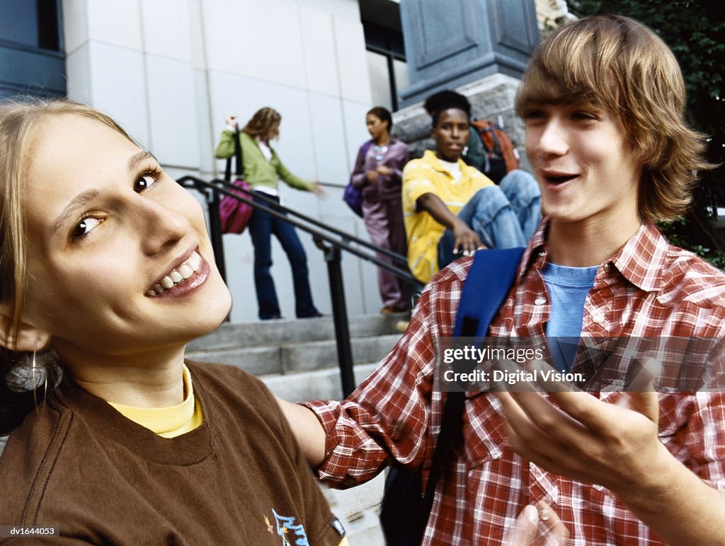 Male Student Chatting Up an Embarrassed Looking Girl at the Bottom of Steps Outside a School Building