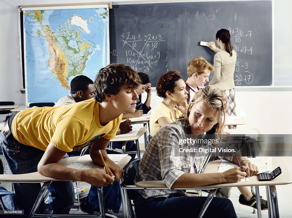 Secondary School Boy Sitting at a Classroom Desk Tries to Peek at the Test Paper of the Boy in Front of Him