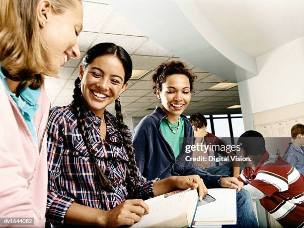 three female students sat on a row of lockers looking at a book, with three male students in the background - the row stock pictures, royalty-free photos & images