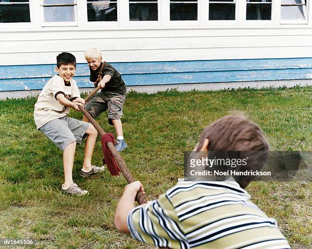 three boys play tug of war in their back yard - war stock-fotos und bilder