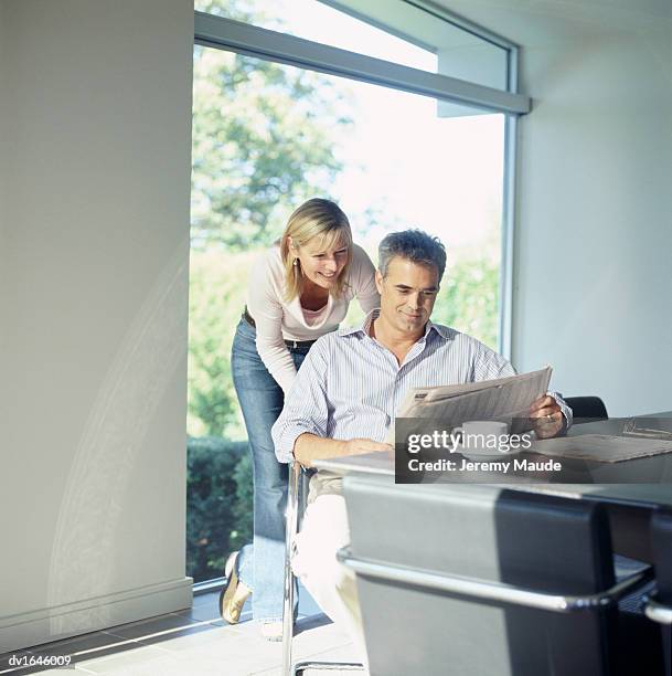 mature man indoors holding and reading a newspaper and woman behind reading too - s night of too many stars america unites for autism programs stockfoto's en -beelden