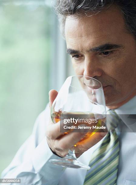 mature businessman sniffing a glass of brandy - bicchiere da brandy foto e immagini stock