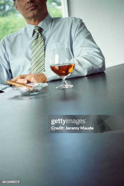 businessman sitting behind a desk with a glass of brandy and a cigar - konjaksglas bildbanksfoton och bilder