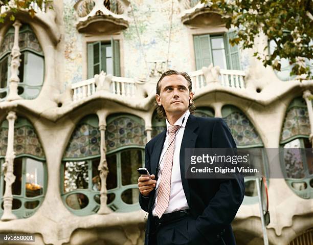businessman stands in front of casa batllo, barcelona, using a headset for his mobile phone - casa stock pictures, royalty-free photos & images