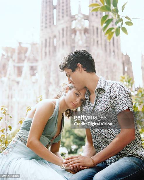 young couple sit holding hands, the sagrada familia in the background, barcelona - familia stockfoto's en -beelden