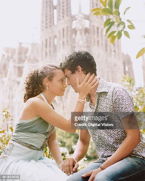 young couple sit face to face holding hands, the sagrada familia in the background, barcelona - familia stockfoto's en -beelden