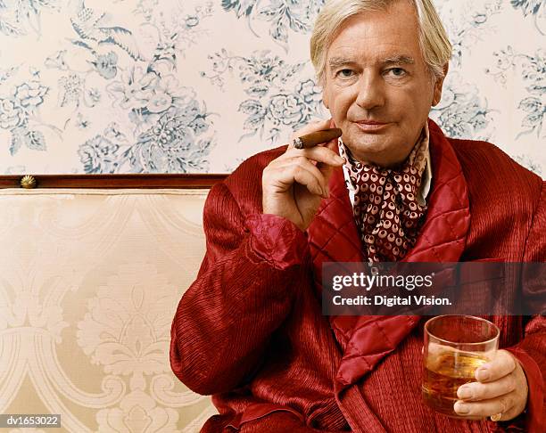 portrait of an aristocratic man in a smoking jacket sitting on a chaise longue holding a glass of whiskey and a cigar - man with cravat stock pictures, royalty-free photos & images