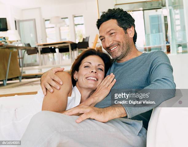 couple laughing together on a sofa in a domestic interior, man with his arm around a woman - camisa sin mangas fotografías e imágenes de stock