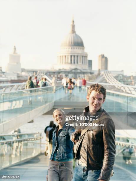 couple walking with the millennium bridge and st pauls cathedral in the background - millennium bridge londra foto e immagini stock
