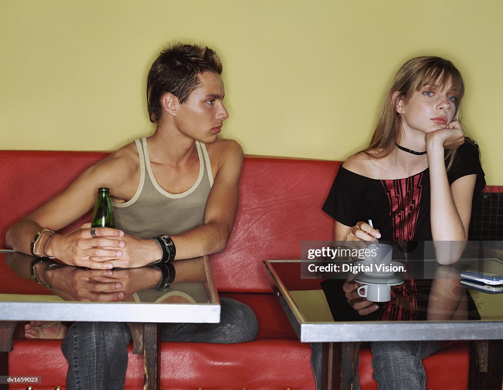 Two Teenage Friends Sit Side-by-Side in a Cafe, Girl Ignoring the Staring Boy