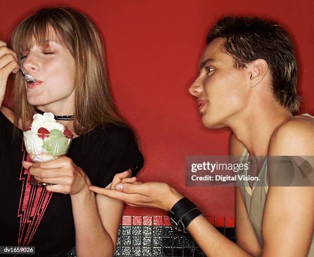 teenage boy ignored by his friend as she sits with her eyes closed eating a cream fruit sundae - boy and girl eating ice cream stock-fotos und bilder