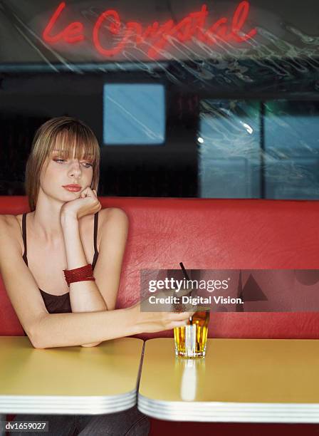 teenager sits alone at a table in a nightclub with a drink under a neon sign - hand on chin thinking stock pictures, royalty-free photos & images