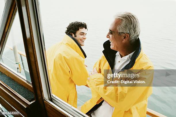 father and his mature son stand on the deck of a sailboat laughing - father son sailing stock pictures, royalty-free photos & images