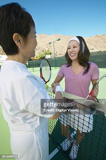 two women shaking hands over a net on a tennis court - tennis court stock pictures, royalty-free photos & images