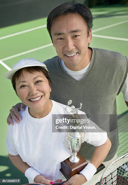 portrait of a mature mother with her mature son on a tennis court holding a trophy - tennis court stock pictures, royalty-free photos & images