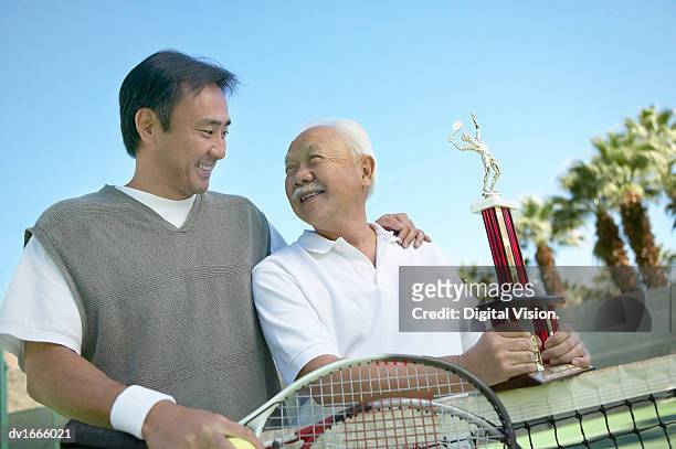 father and son standing on a tennis court, with the father holding a trophy - cas awards imagens e fotografias de stock