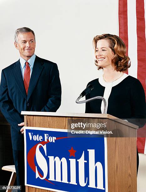 woman giving a speech at a political rally watched by a male political colleague - being watched stockfoto's en -beelden