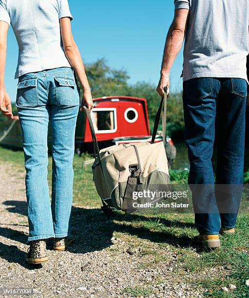 couple walking towards a boat and  carrying a heavy bag between them - voyage15 photos et images de collection