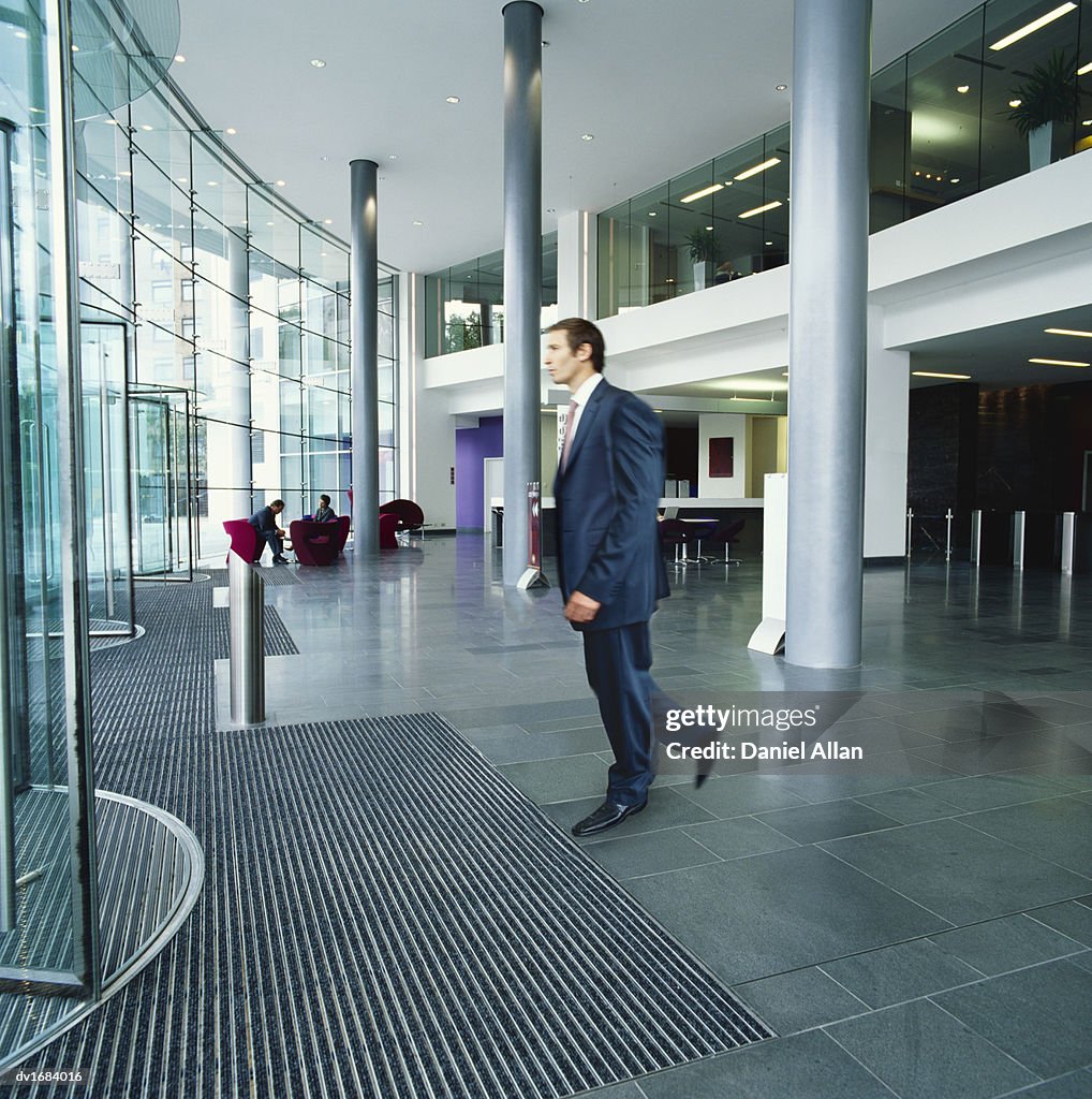 Businessman Walks Towards Revolving Doors as He Leaves an Office Building