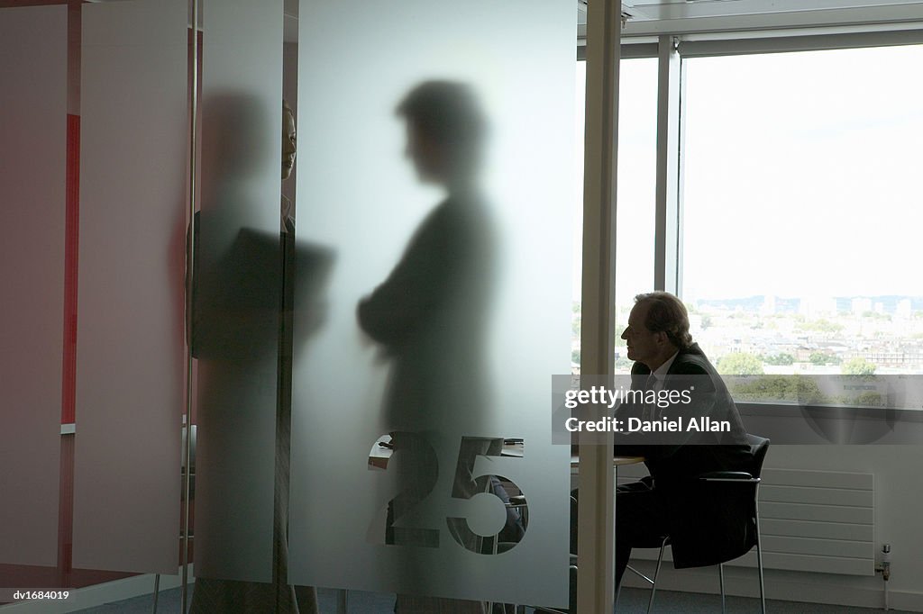 Businessman in a Meeting and Silhouettes of Businesswomen Talking Behind Frosted Glass