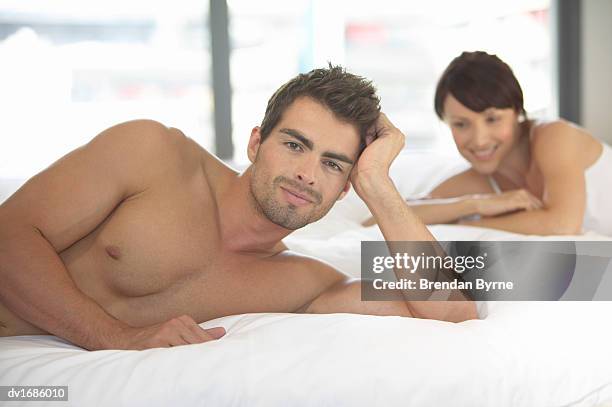 thirty something man lying on a bed and his girlfriend behind him - brendan stock-fotos und bilder