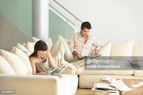 thirty something couple on a sofa reading magazines - brendan stock-fotos und bilder