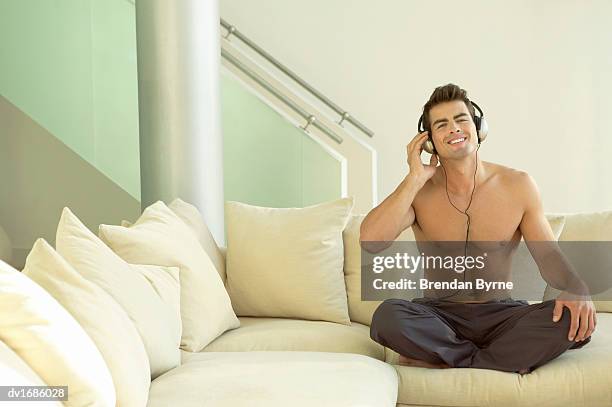 thirty something man sitting on a sofa listening to music on headphones - brendan stock-fotos und bilder