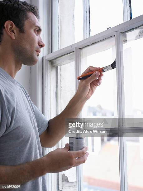 man holding a paint tin and a paintbrush, painting a window frame - holz streichen stock-fotos und bilder