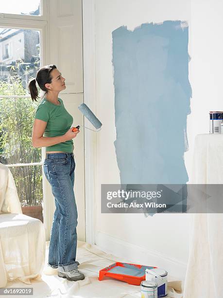 woman contemplating paint she has freshly applied to a wall - jury loisirs photos et images de collection