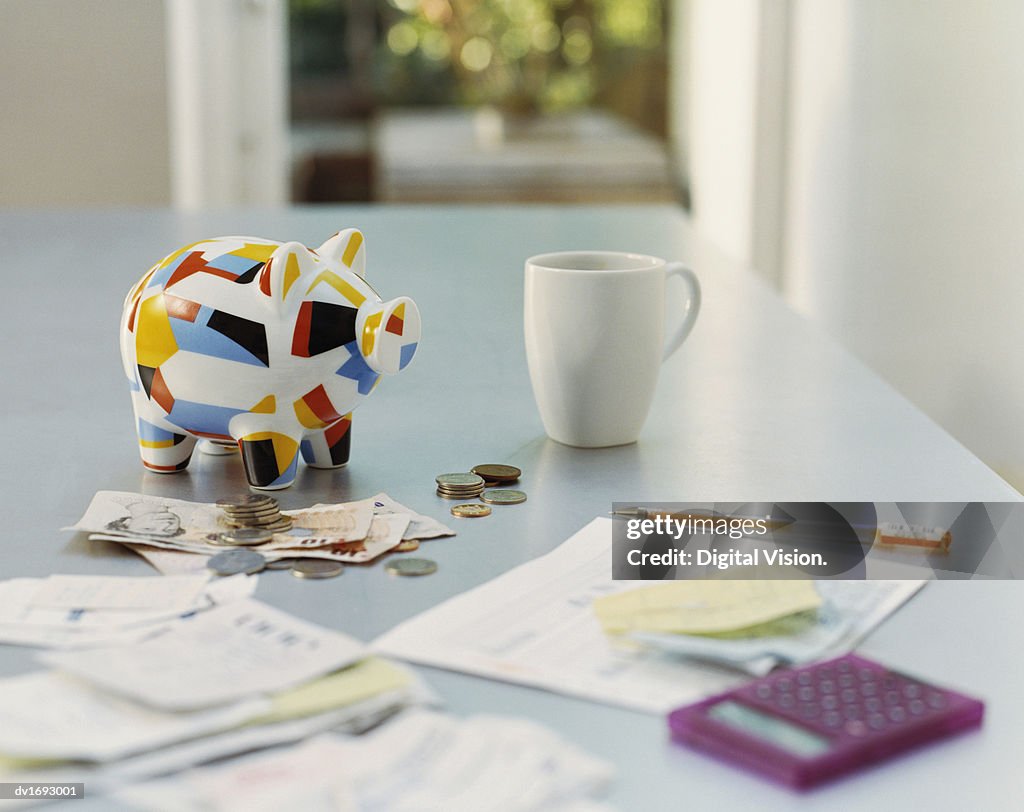 Piggybank, British Currency, Calculator, Receipts and a Mug on a Table