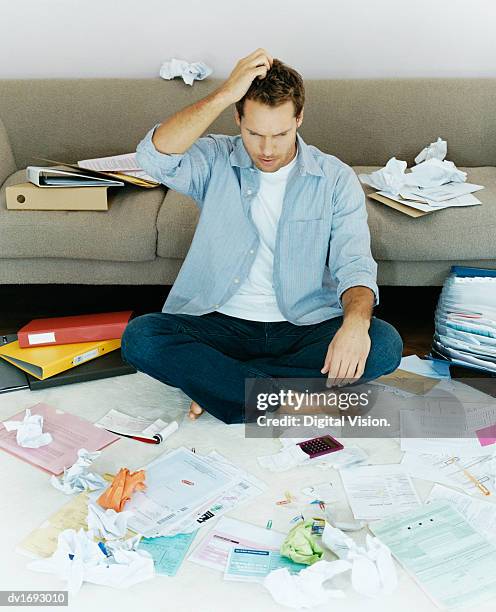 man sits on a rug surrounded by bills and folders, scratching his head - faze rug stock pictures, royalty-free photos & images