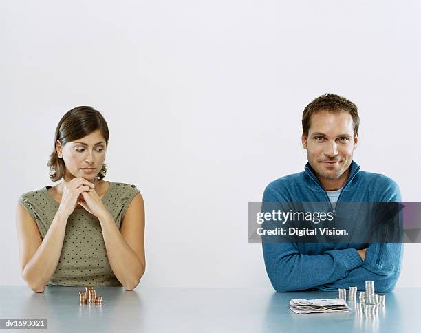 man and woman sit next to each other with a pile of money in front of them, woman looking jealous at man's pile - envy stock pictures, royalty-free photos & images