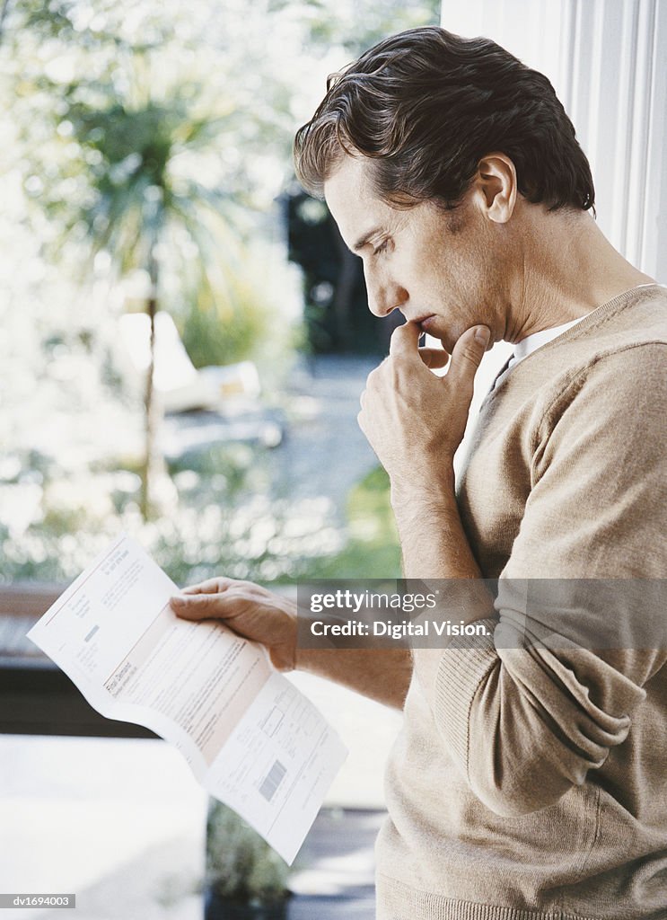 Pensive Man Stands Indoors Examining a Bill